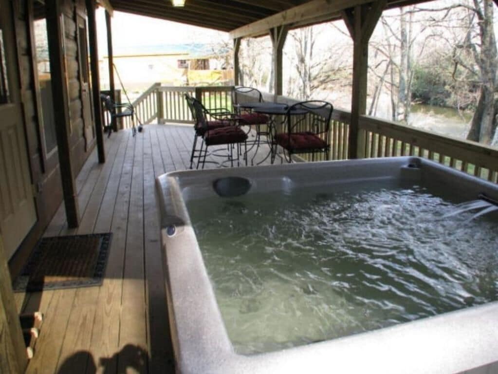A hot tub on a wooden deck with outdoor furniture and a view of trees and a building in the background.