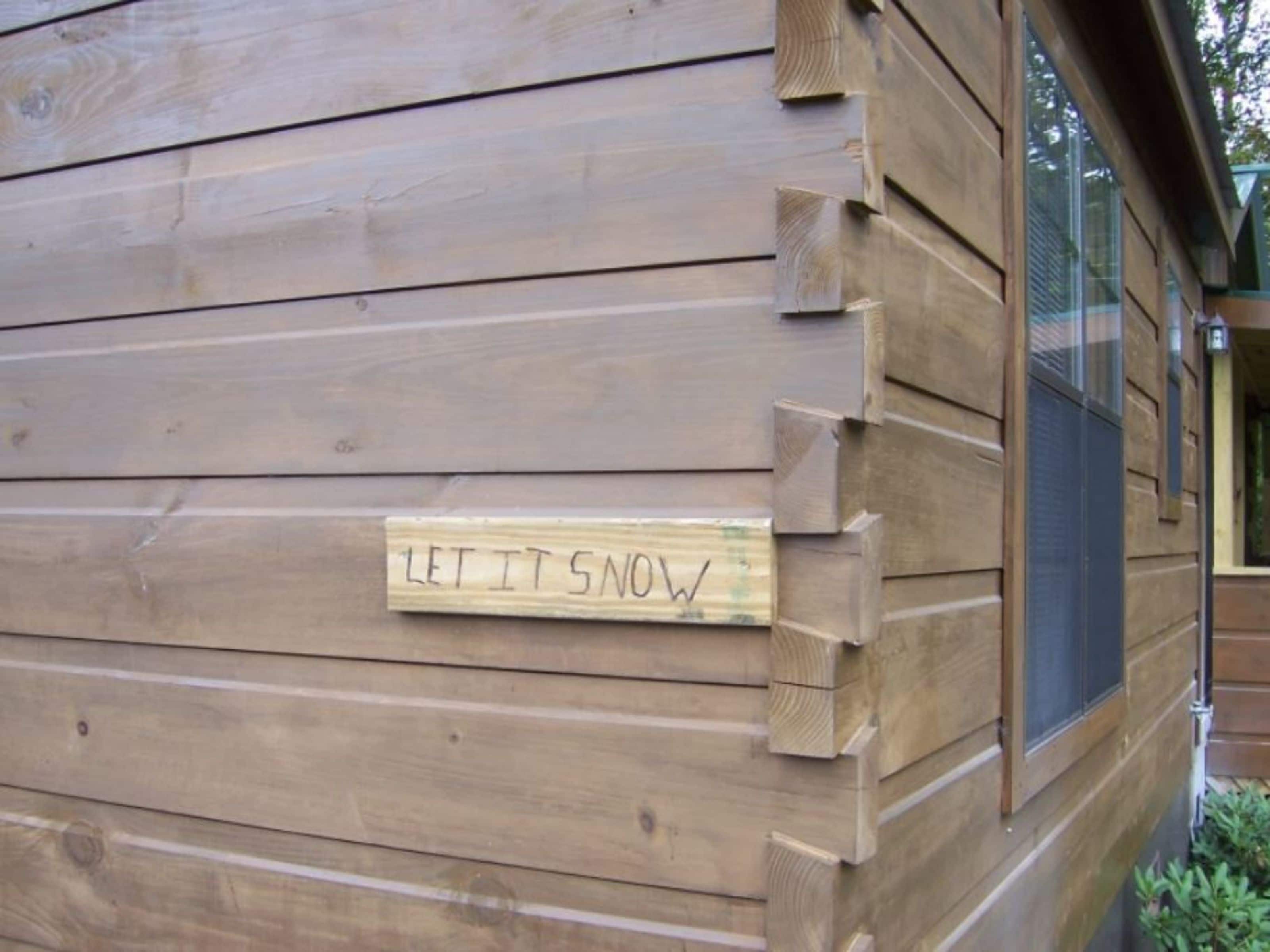 Une cabane en bois avec une pancarte sur laquelle on peut lire : « QU’IL NEIGE ».