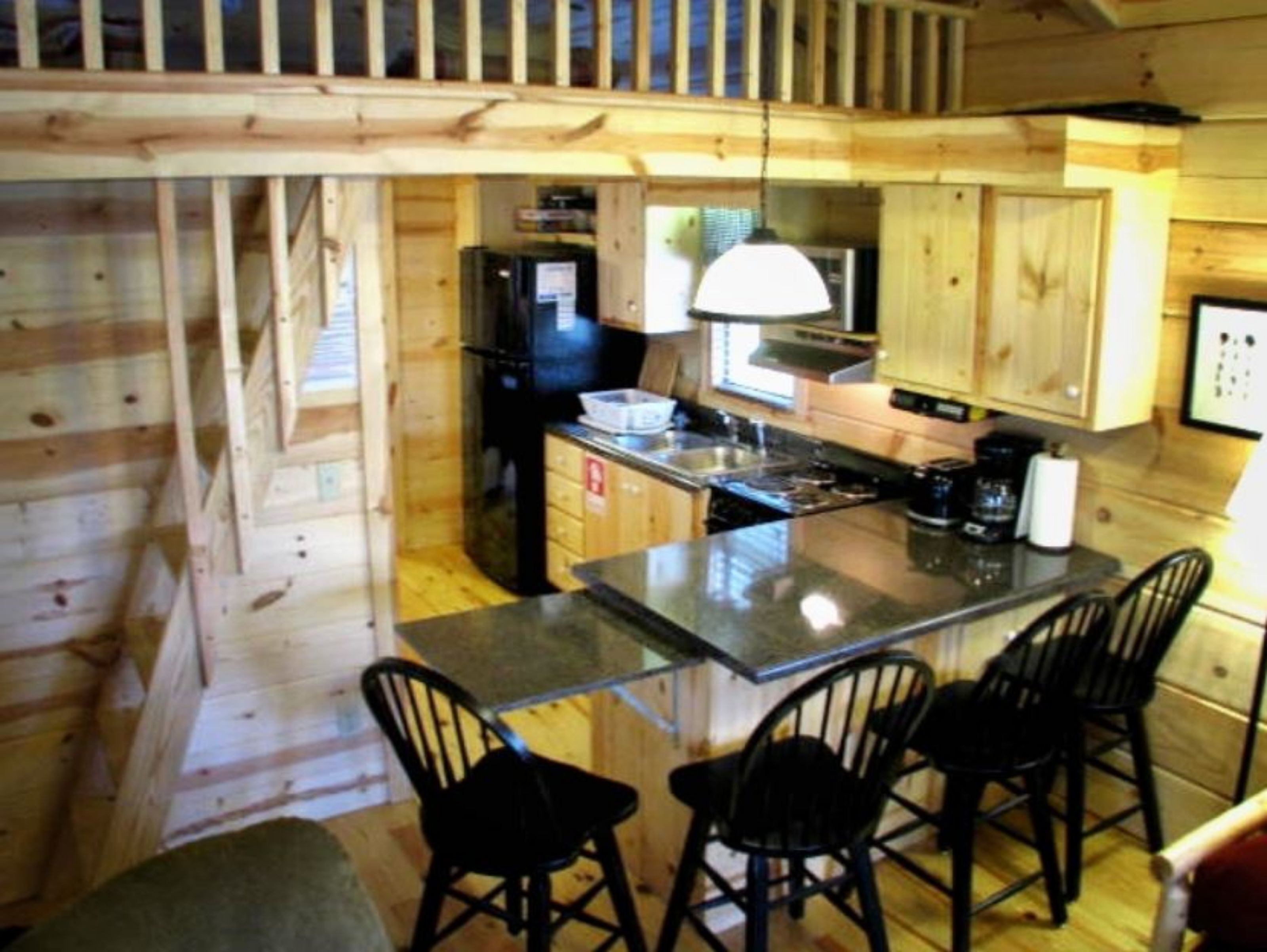 A compact kitchen with wooden walls, a black refrigerator, a stove, and a small island with bar stools.
