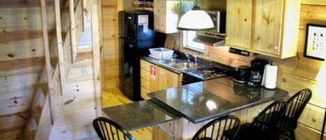 A compact kitchen with wooden walls, a black refrigerator, a stove, and a small island with bar stools.