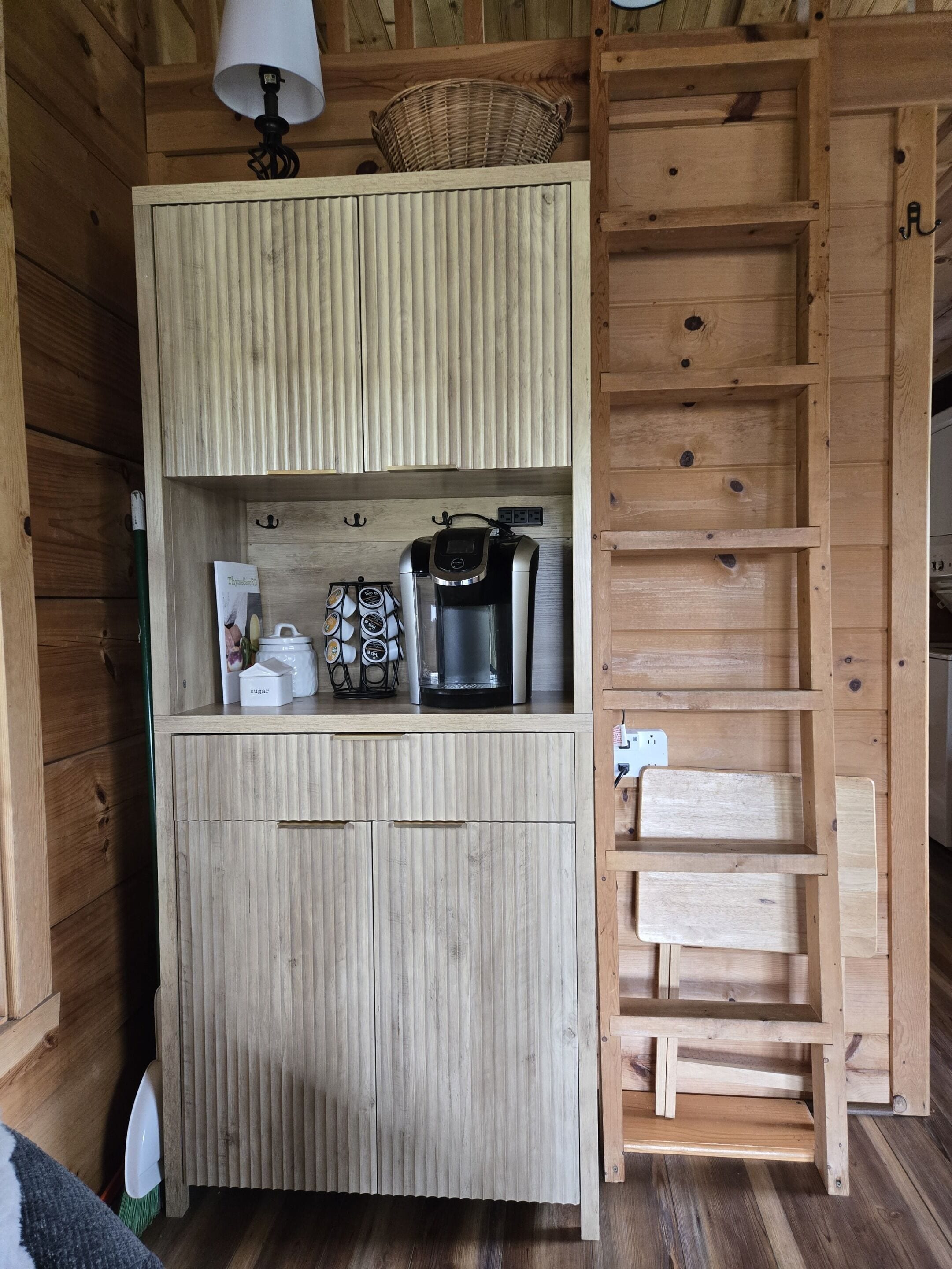A wooden kitchen with a coffee maker, sugar containers, and a basket.