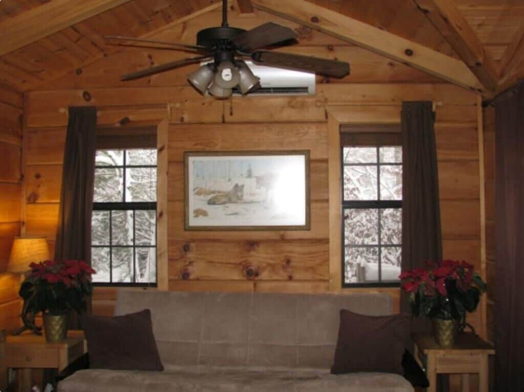 A log cabin room with a ceiling fan, a framed picture on the wall, a sofa, and two side tables with flower vases.