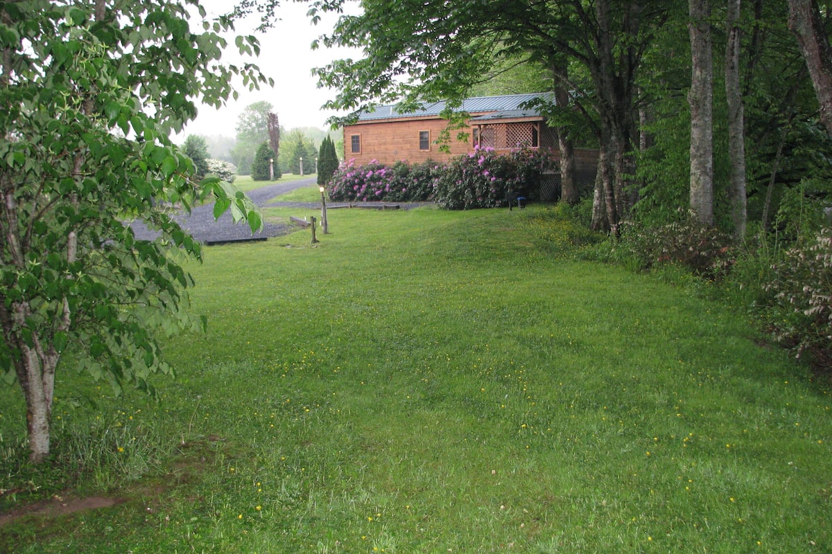 A grassy area with a brick building, trees, and a pathway.