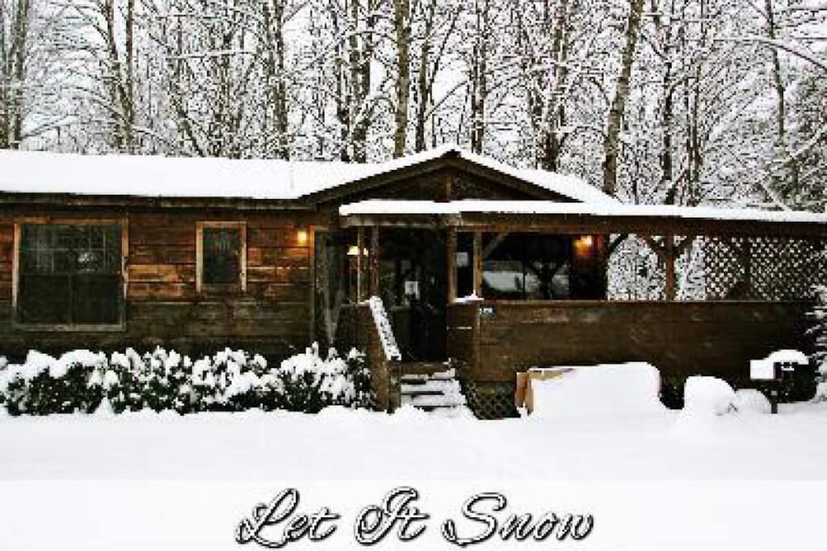 A wooden cabin with a snow-covered roof and a porch, surrounded by a snowy landscape.