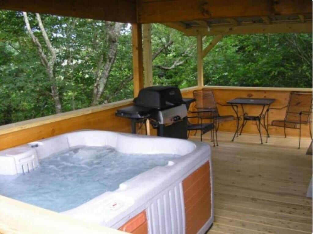 A hot tub on a wooden deck with a grill and chairs.