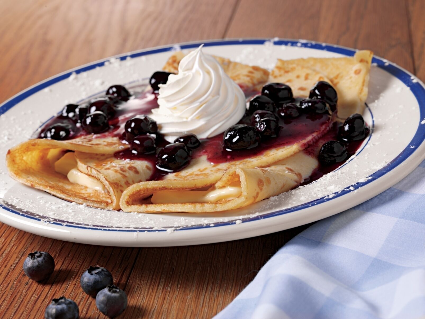 A plate of crepes with blueberries and whipped cream.