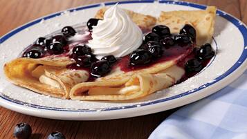 Une assiette de crêpes garnies de myrtilles et de crème fouettée.