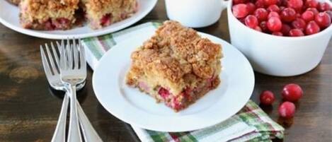 Un dessert aux fruits rouges, une tasse blanche et un bol de fruits rouges sur une table.