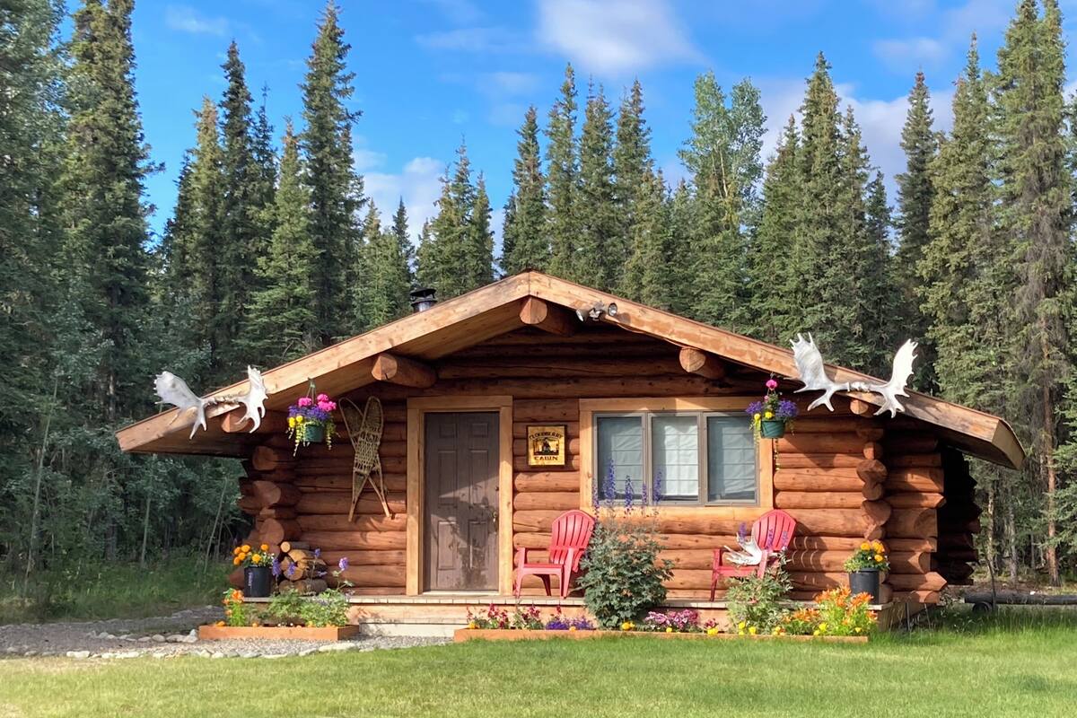 Una cabaña de troncos con un porche, dos sillas Adirondack rojas y un letrero que dice 'CLOUETTEAU'.