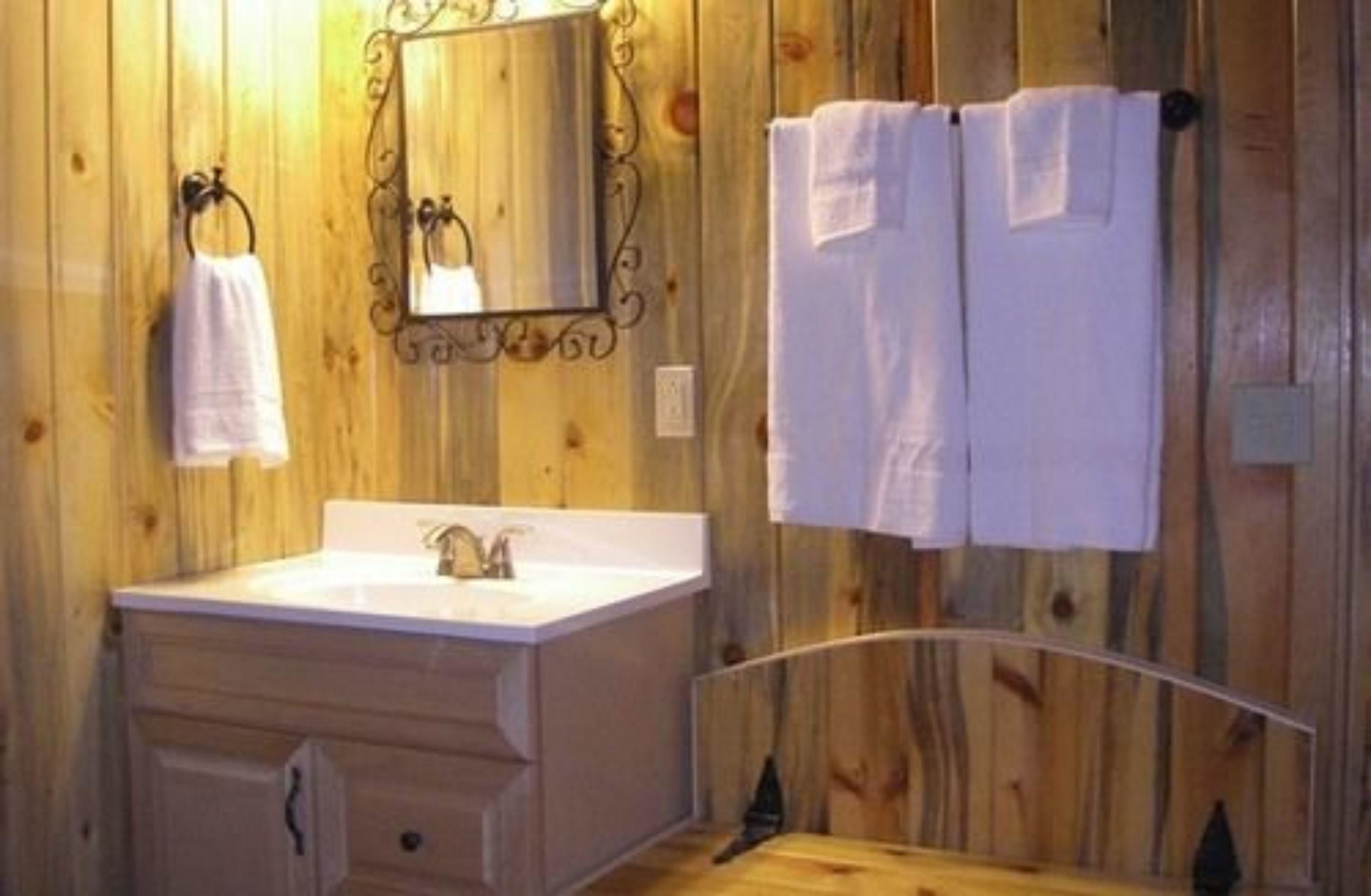 A wooden-paneled bathroom with a white sink, a mirror, and two towels hanging on a rack.