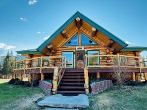 A log cabin with a steep staircase leading to a porch, surrounded by a wooden fence and a brick wall. - Cloudberry Cabin (Tok)