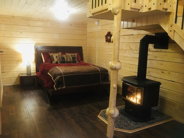 A cozy wooden room with a bed, a wooden staircase, and a wood-burning stove.