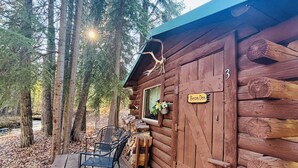 Een rustieke blokhut met een houten terras, een raam met bloembak en een bordje met de tekst 'Bears Den'.