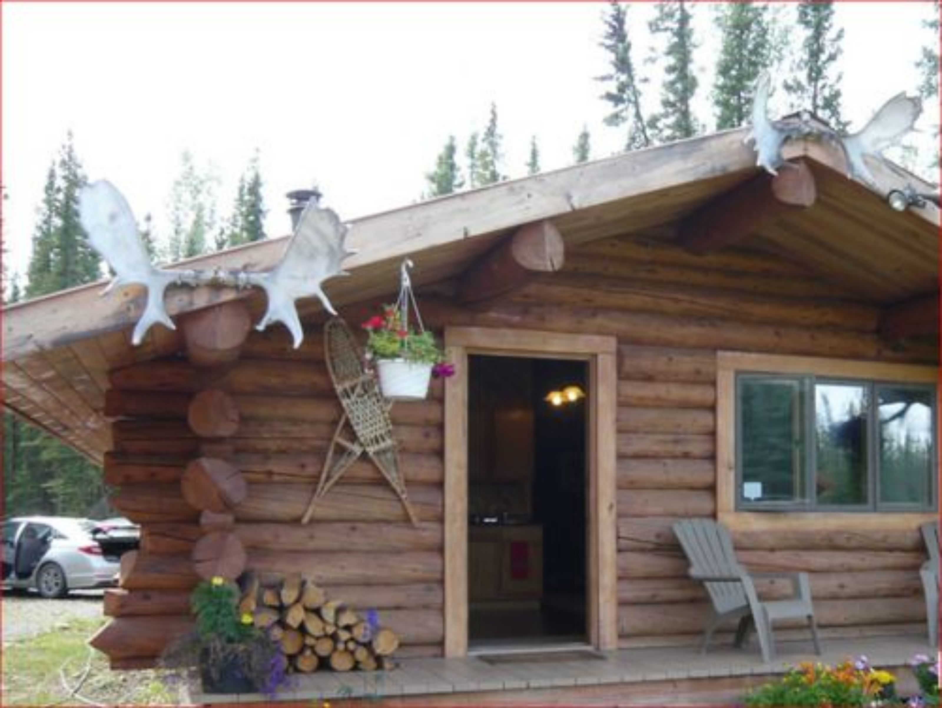 Eine Blockhütte mit Veranda, einem Sessel, einem hängenden Blumentopf und einem Holzstapel.