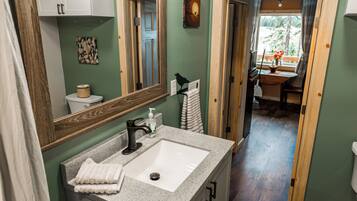 A bathroom with a white sink, a mirror, and a wooden door leading to a dining area.