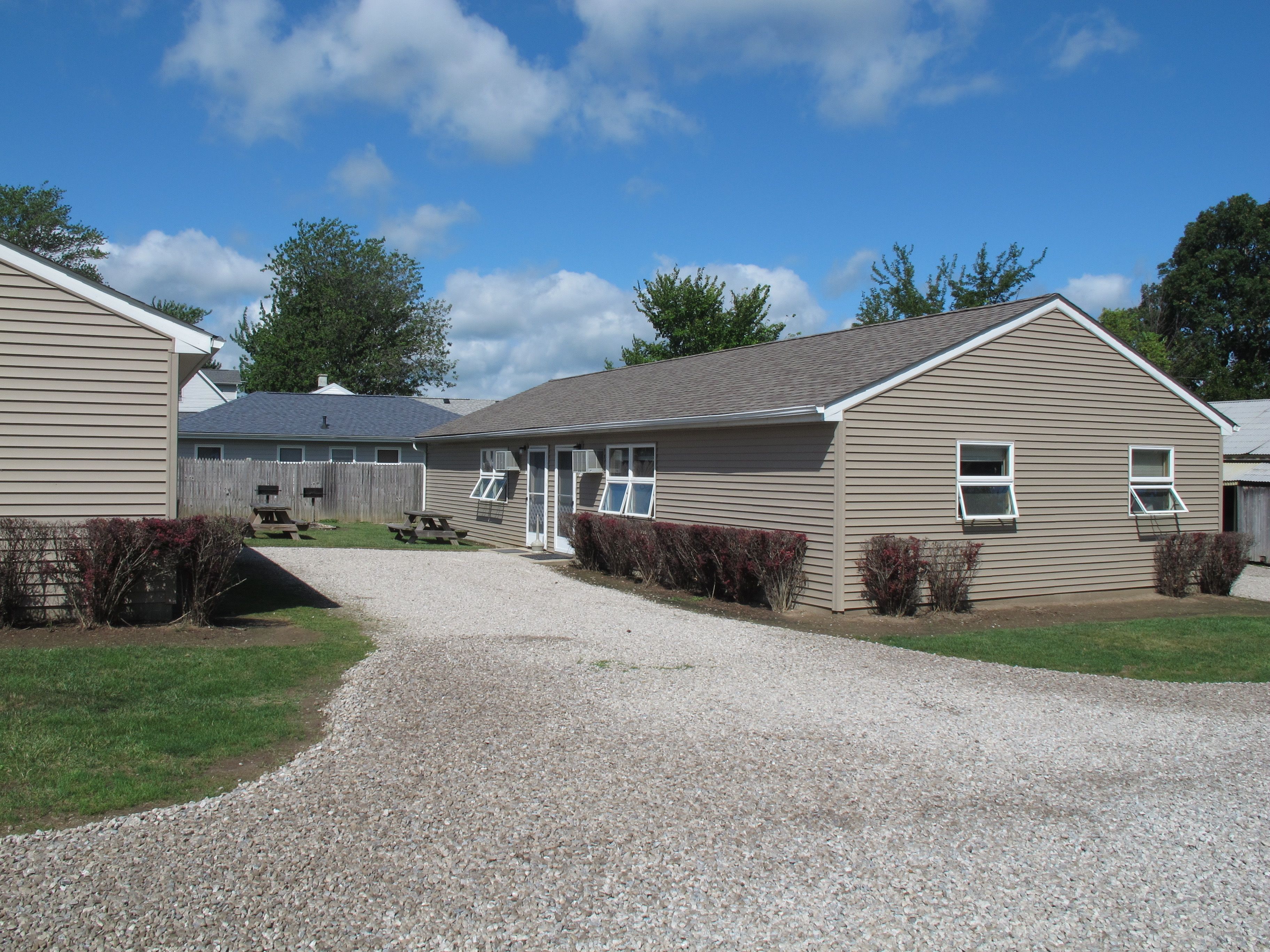A two-story building with a gravel driveway leading to a covered patio area.