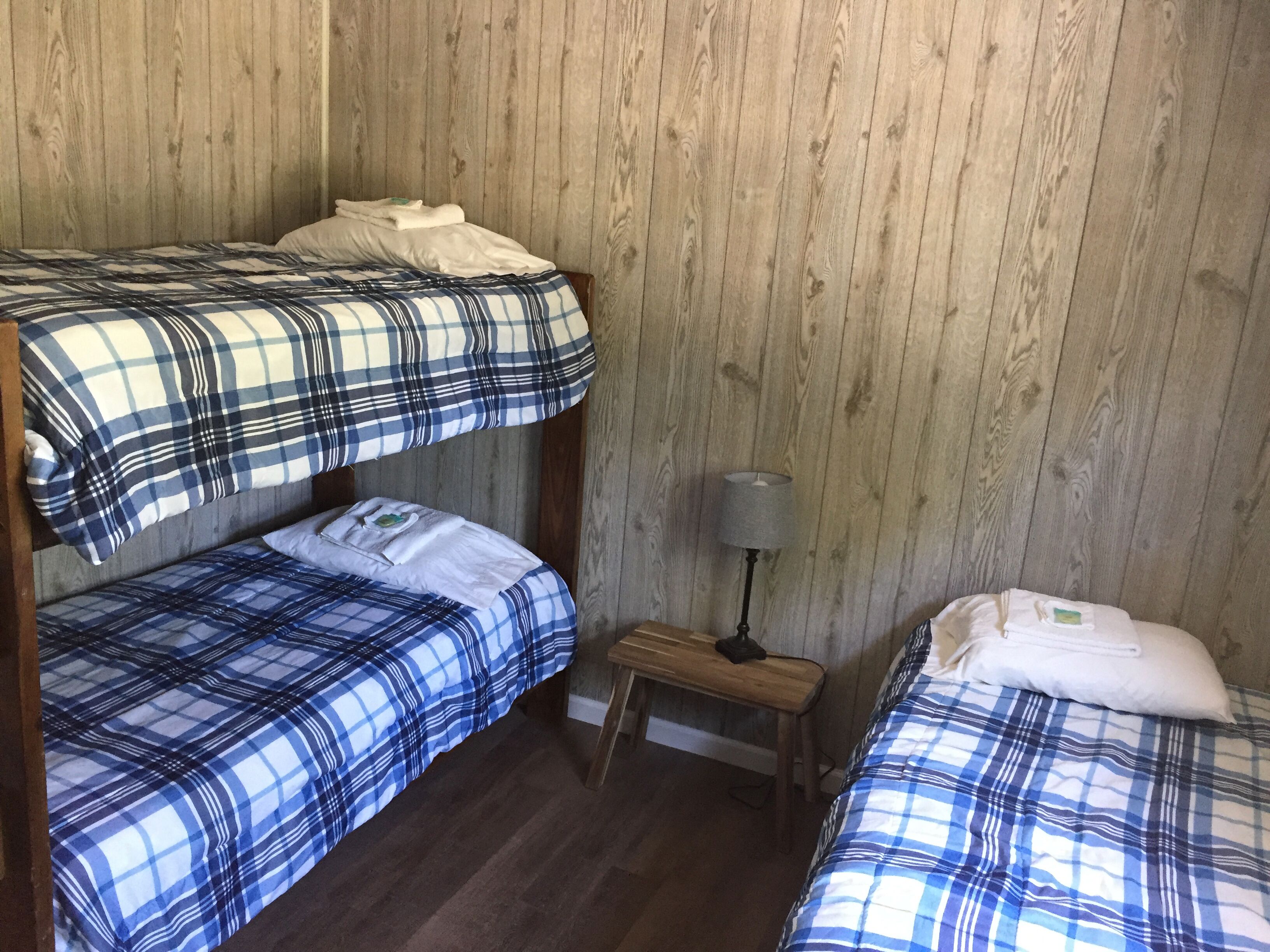 A room with two bunk beds, a small wooden nightstand with a lamp, and a single bed.