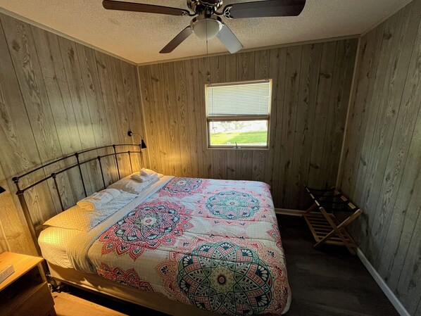 Une chambre à coucher avec un lit, un ventilateur de plafond, une fenêtre et un mur en bois.
