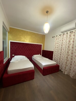 A hotel room with two beds, a red headboard, a window, and a floral curtain. - Hotel Red Apple (Mbrostar Ura)