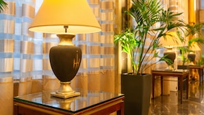 Un hall d’entrée avec une lampe sur une table en verre, une plante en pot et un mur orné d’un motif.