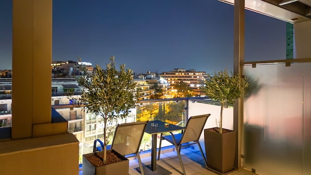 Un balcon avec deux chaises et deux plantes en pot, donnant sur une vue de la ville au crépuscule.