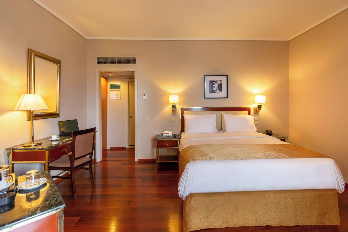 A hotel room with a bed, desk, chair, and bedside lamps.