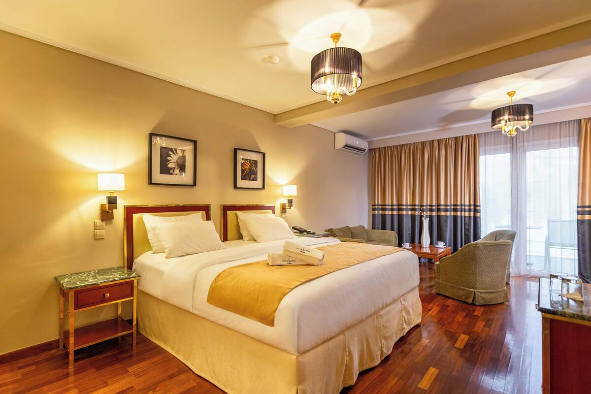 A hotel room with a large bed, two bedside tables, a chair, and a desk with a lamp.