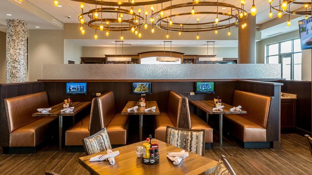 A restaurant with booths and tables, a stone pillar, and a TV screen. - Holiday Inn Lexington - Hamburg by IHG (Lexington)