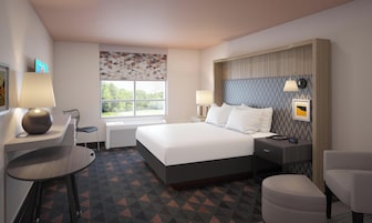 Habitación de hotel con cama, mesitas de noche, escritorio, una silla y ventana con vistas.