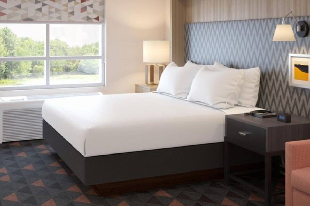 A hotel room with a bed, a desk, a chair, a small table, and a window with a view of greenery.