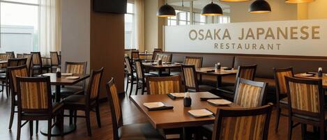 Interior de restaurante con mesas y sillas de madera, un letrero grande que dice 'OSAKA JAPANESE RESTAURANT' e iluminación colgante.