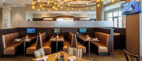 A restaurant with booths and tables, overhead lighting, and a TV screen.
