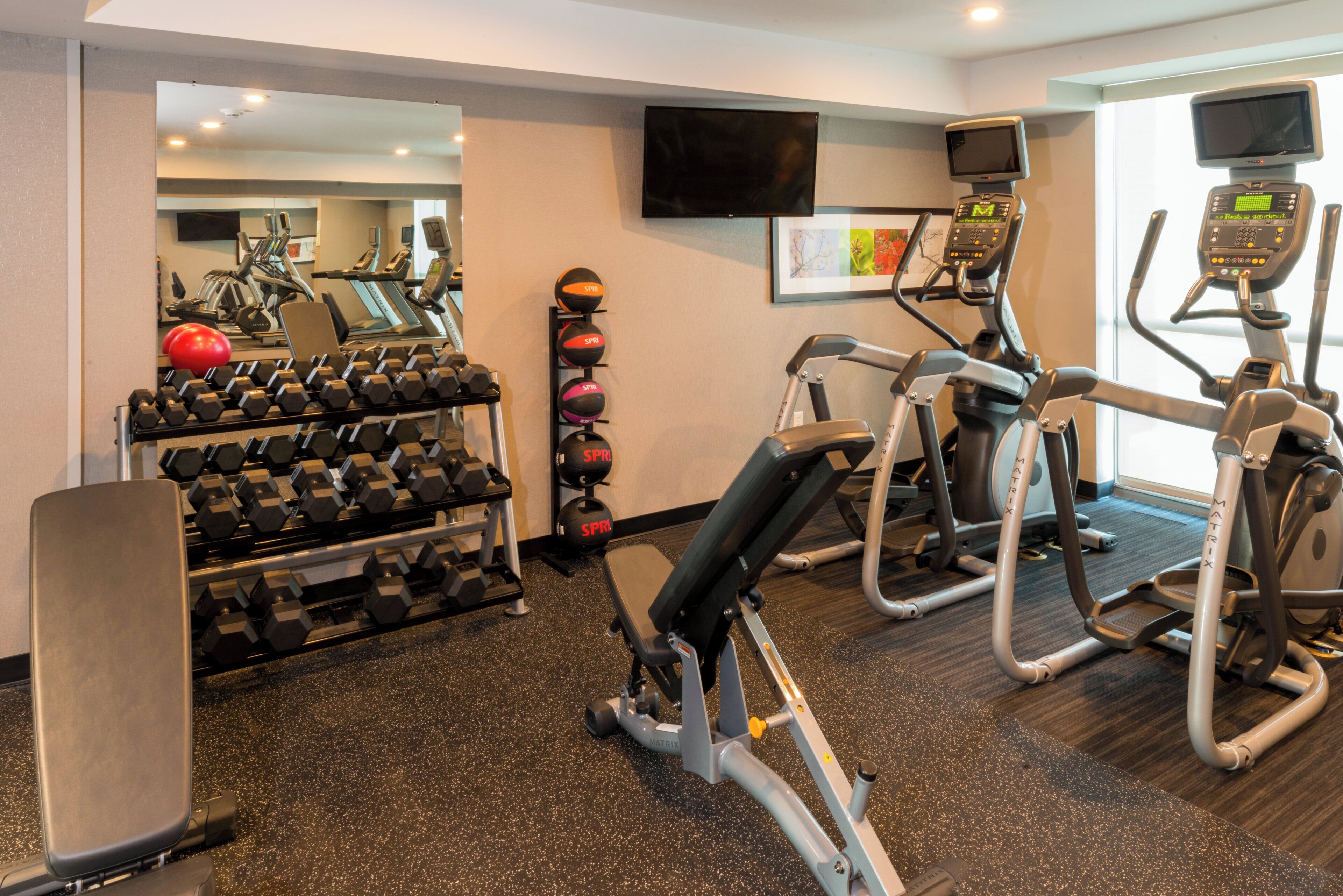 A gym with various exercise equipment, including dumbbells, a bench, and cardio machines.