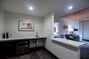 Een hotelkamer met een kitchenette, een bed, een bureau en een televisie.