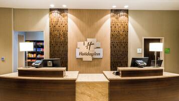 A Holiday Inn reception desk with two counters, a wall-mounted sign, and a snack bar in the background.