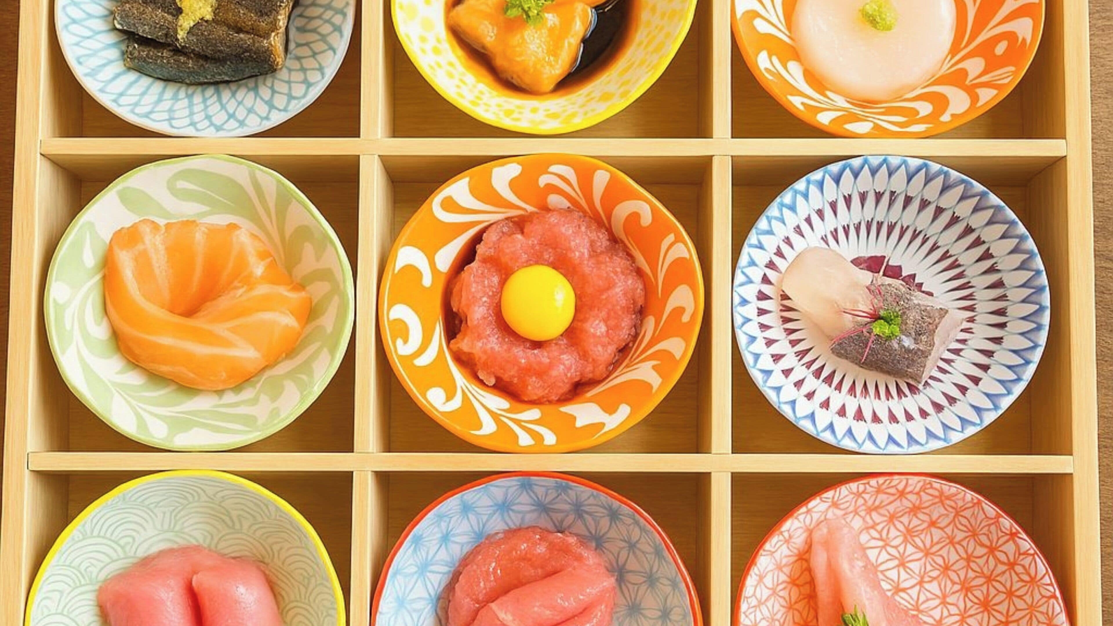 A wooden tray with nine bowls of various Japanese dishes.
