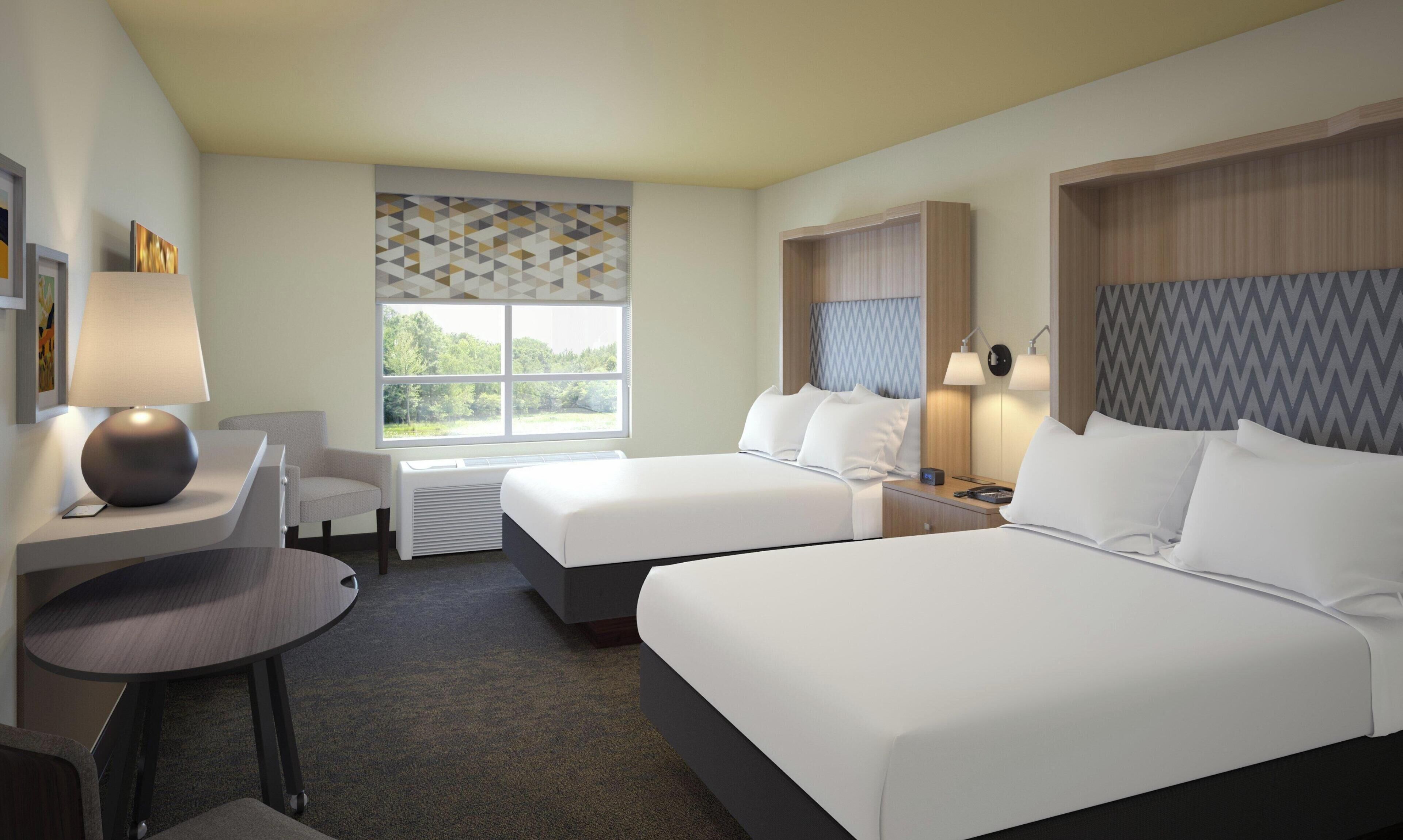 A hotel room with two beds, a desk, a chair, and a window with a view of trees.