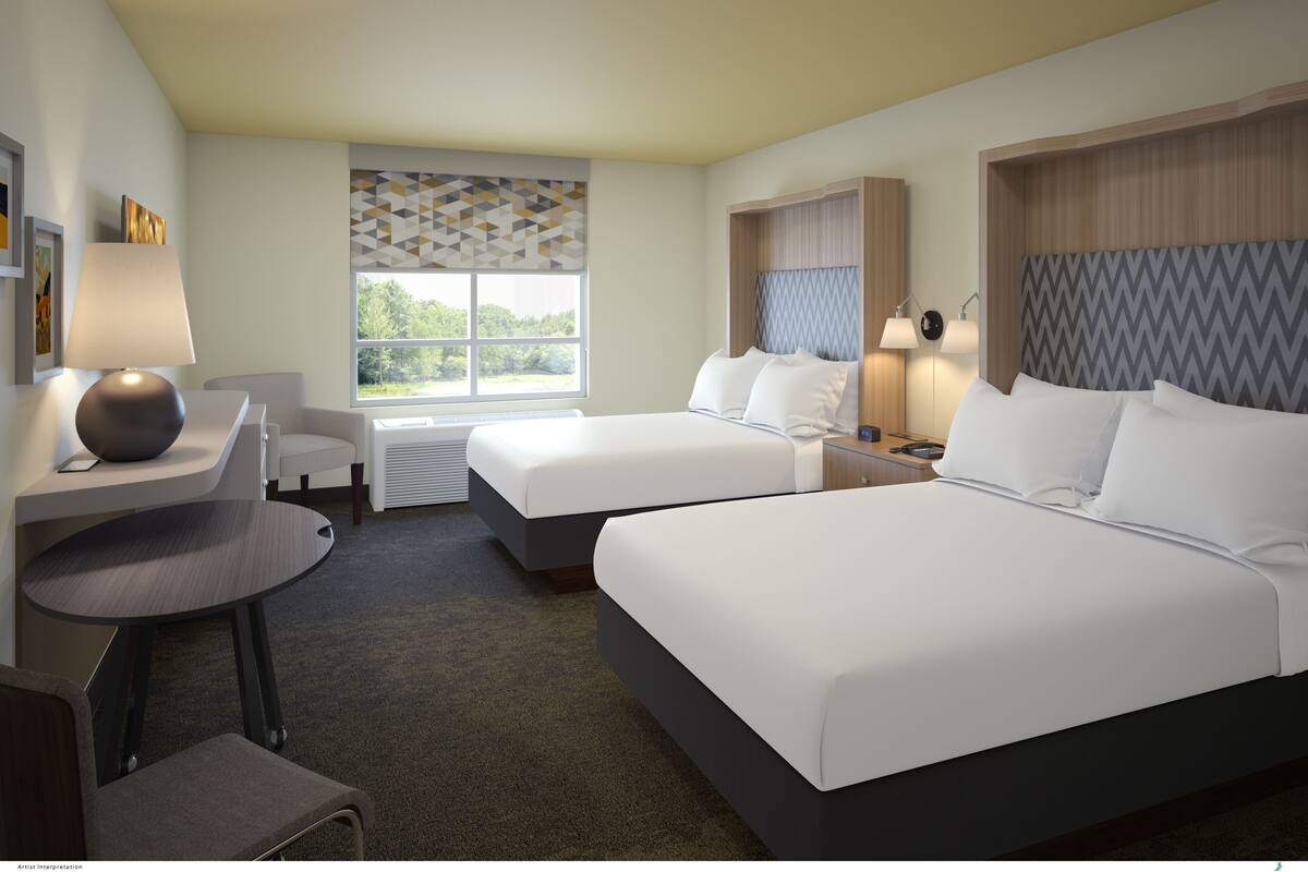 A hotel room with two beds, a desk, a chair, a lamp, and a window with a geometric patterned blind.