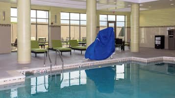 Una piscina interior con agua cristalina, rodeada de sillones de descanso y una zona de estar cubierta.