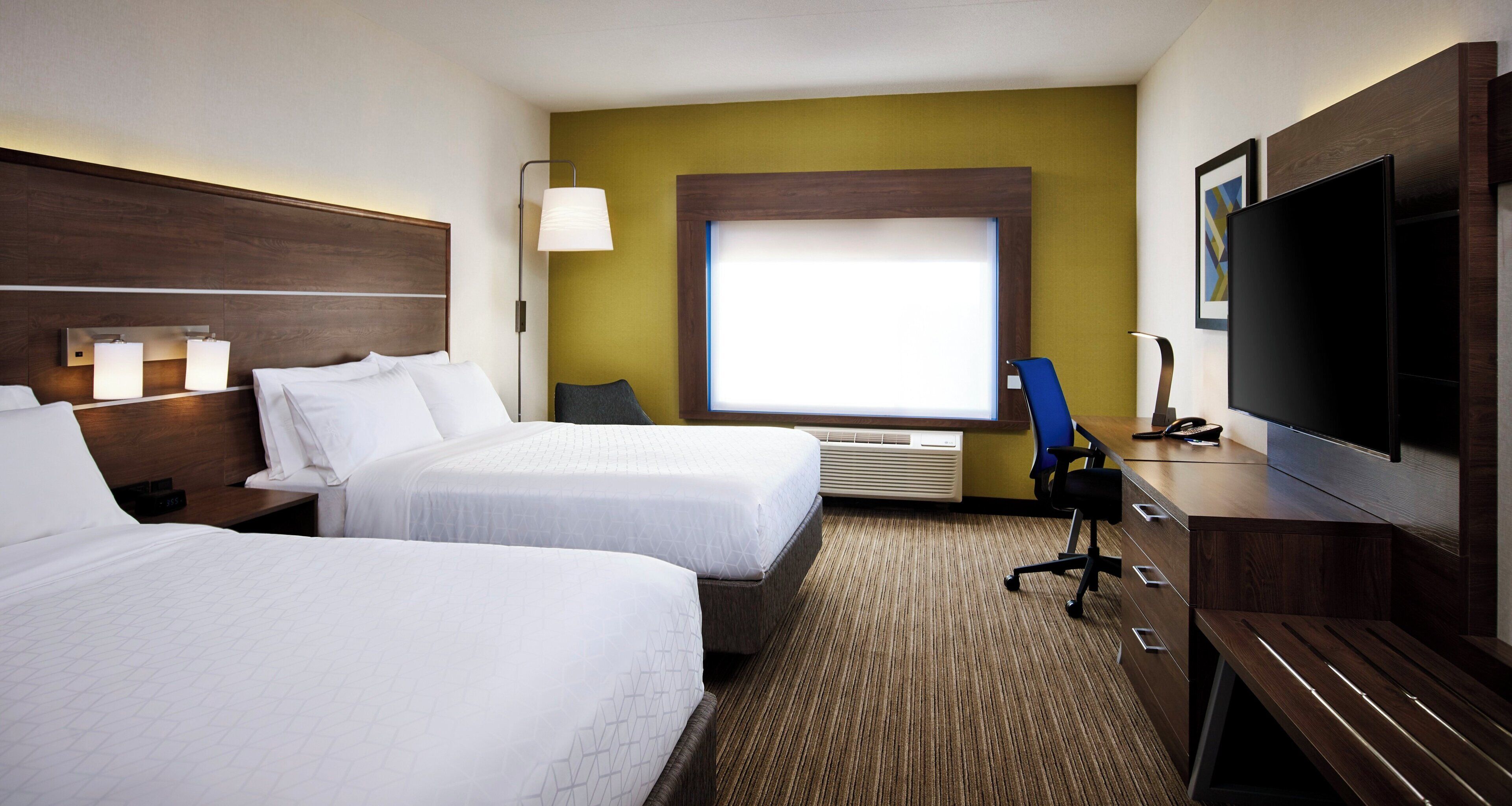 A hotel room with two beds, a desk, a television, and a window with blinds.