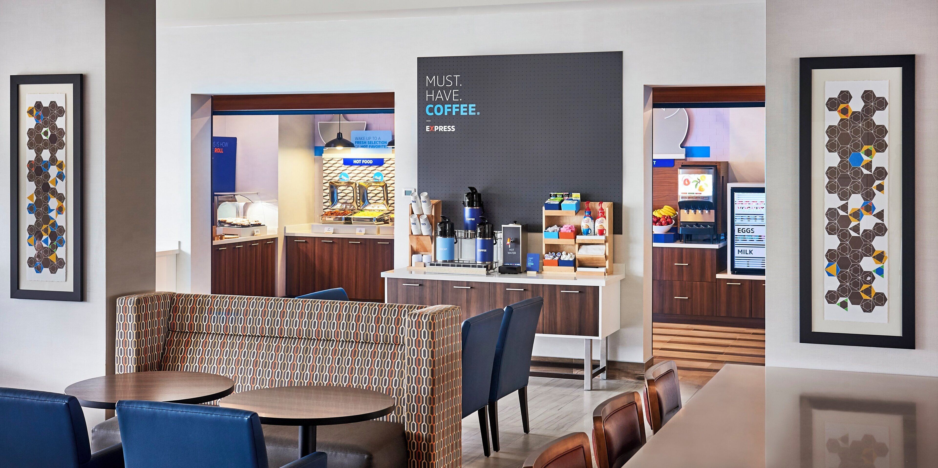 Un moderno hall de hotel con estación de café, zona de estar y obras de arte enmarcadas.