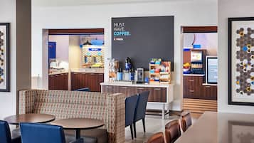 Un moderno hall de hotel con estación de café, zona de estar y obras de arte enmarcadas.