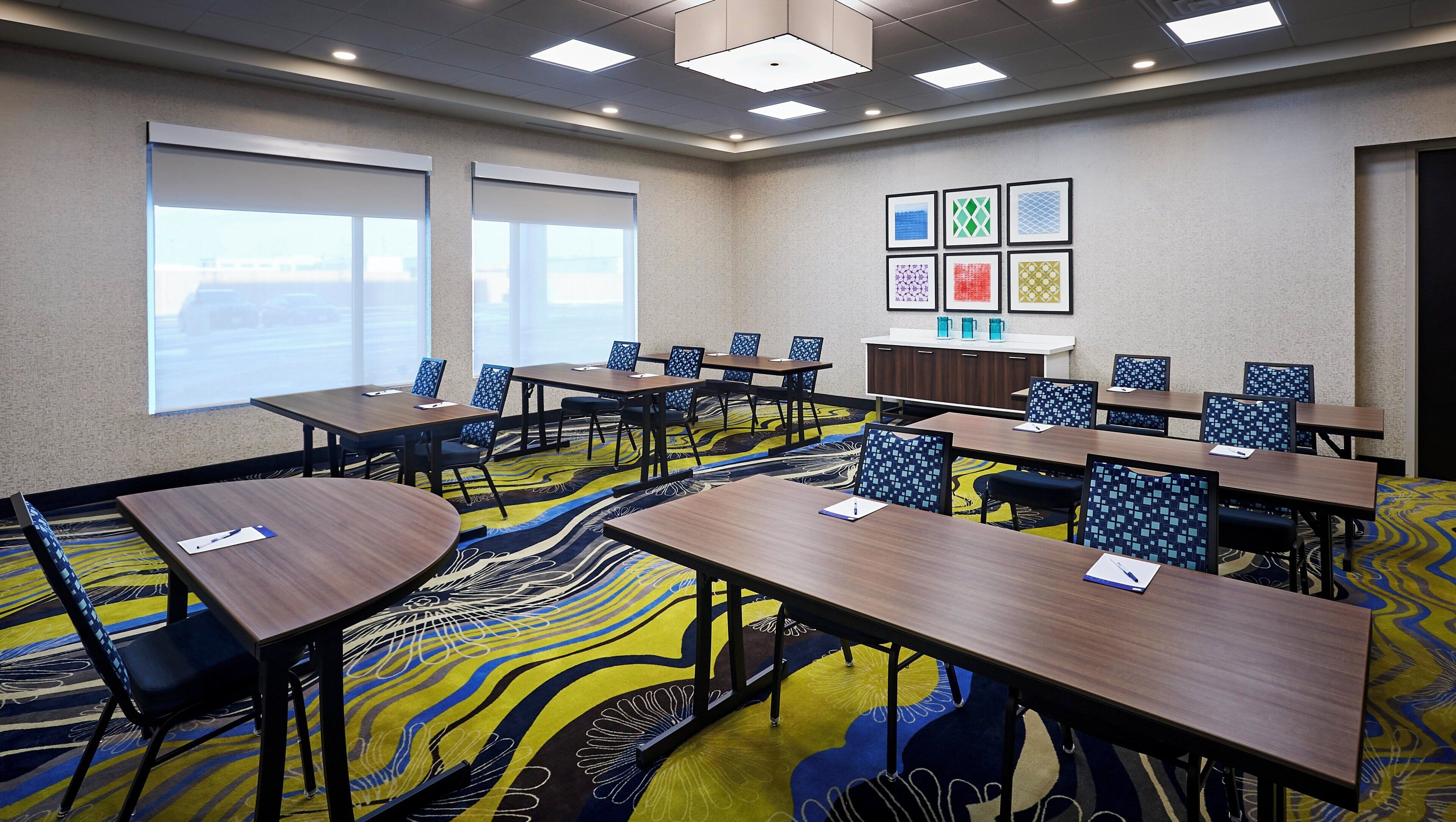 Une salle de conférence dotée de plusieurs tables et chaises, d’un sol recouvert de moquette et offrant une vue sur l’extérieur grâce à de grandes fenêtres.