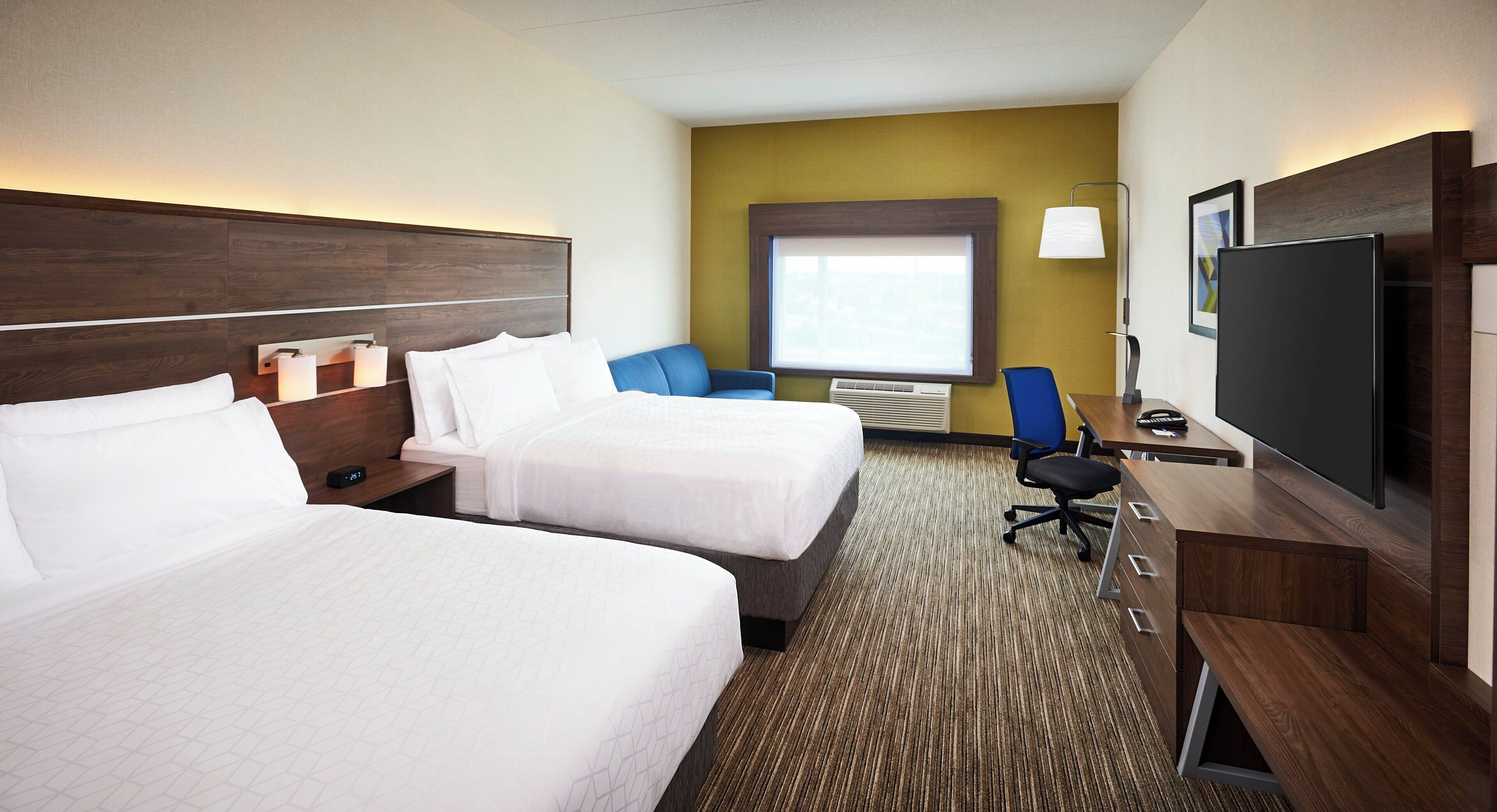 A hotel room with two beds, a desk with a chair, a television, and a window.