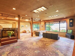 A spacious room with a carpeted floor, a wooden console table with a plant, a sofa set, a television, and a clock on the wall. - Ohamaso (Toba)
