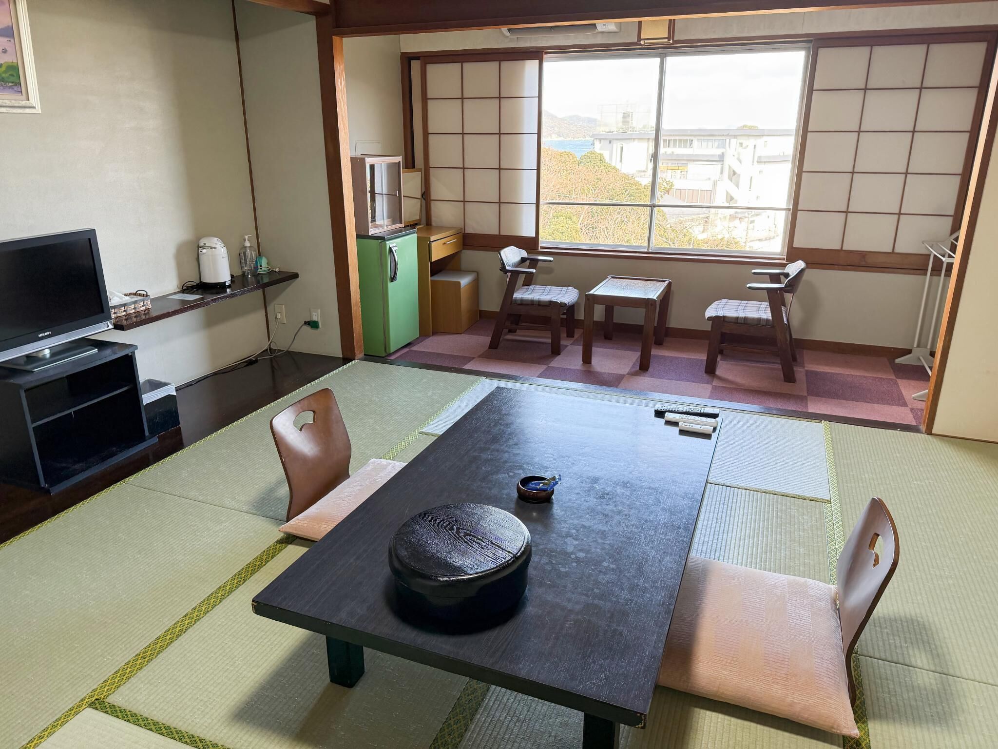 Una habitación japonesa tradicional con suelo de tatami, una mesa baja con una bandeja negra y un televisor sobre un estante.