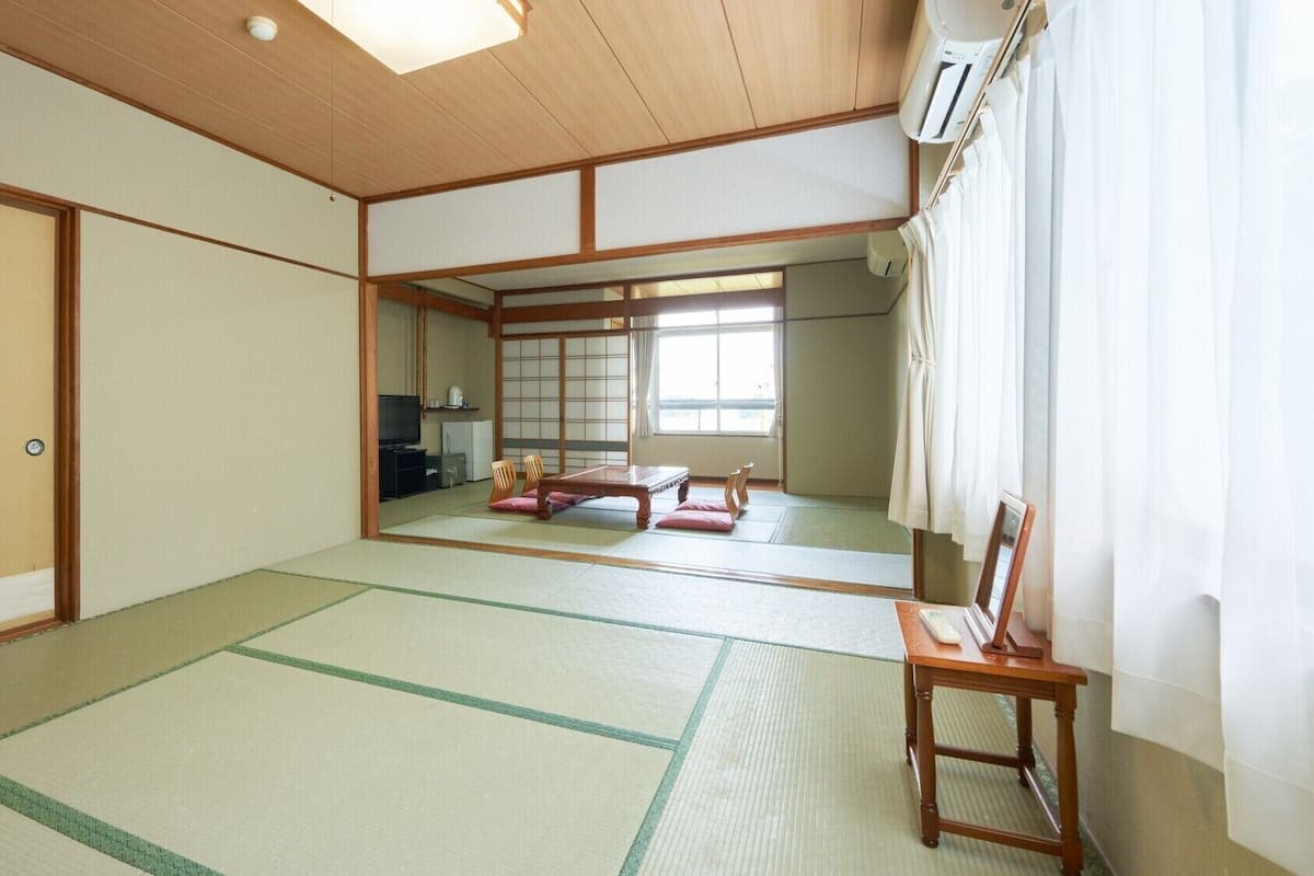 Une pièce de style japonais traditionnel, avec un sol recouvert de tatamis, une porte coulissante, un téléviseur et un futon servant de lit.