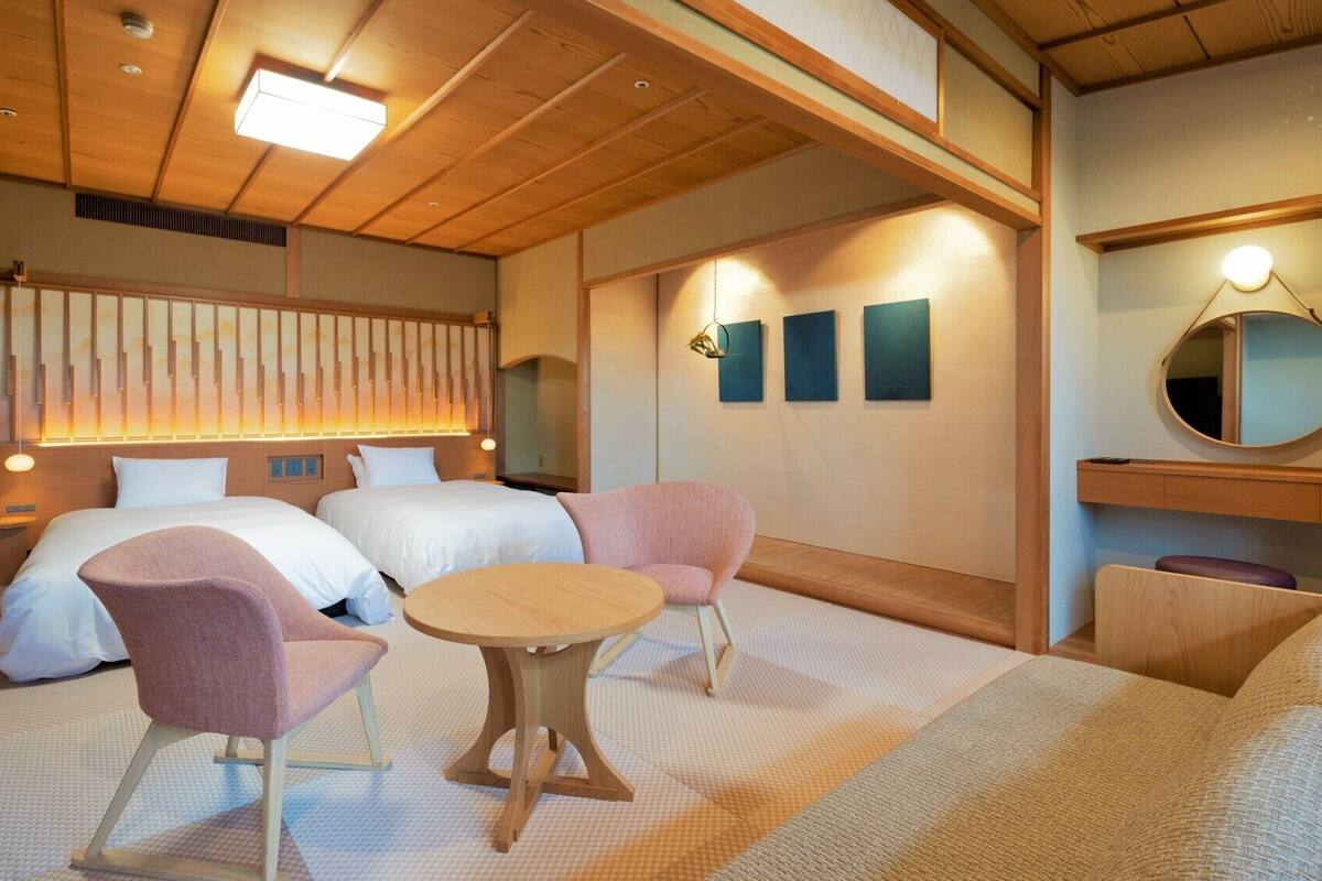 A hotel room with two beds, a sitting area with a table, and a mirror.