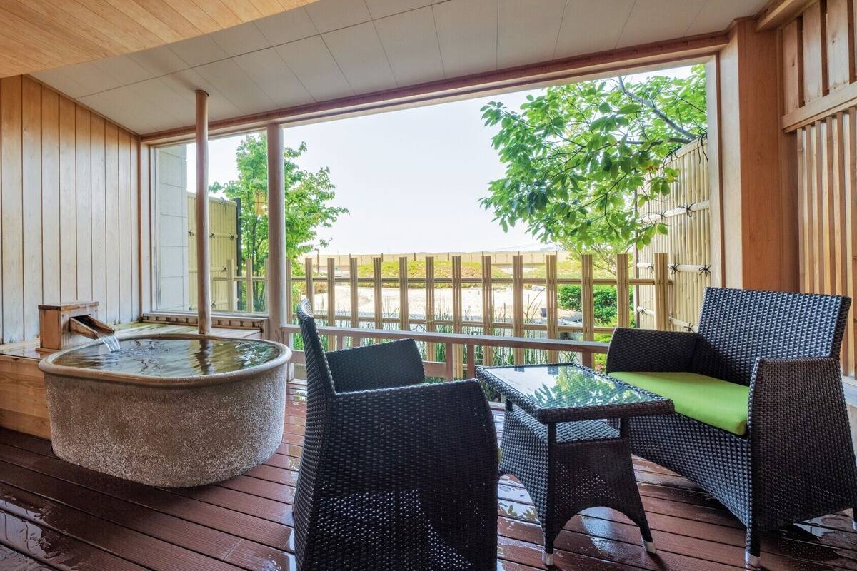 A wooden deck with a hot tub, wicker furniture, and a view of trees and a fence.