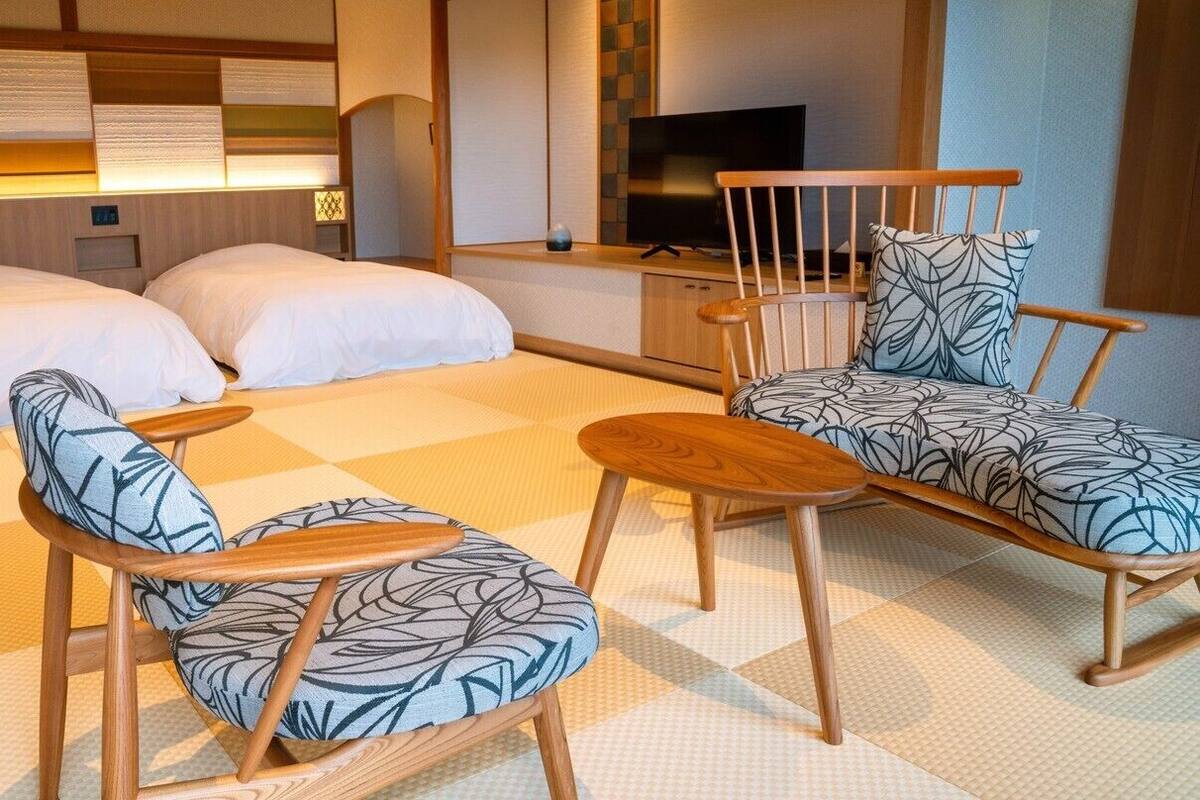 A hotel room with a bed, two chairs, a small table, a TV, and a wall with a patterned design.